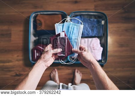Preparing For Travel In New Normal. Man Packing Passport, Face Masks And Hand Sanitizer. Themes Pers