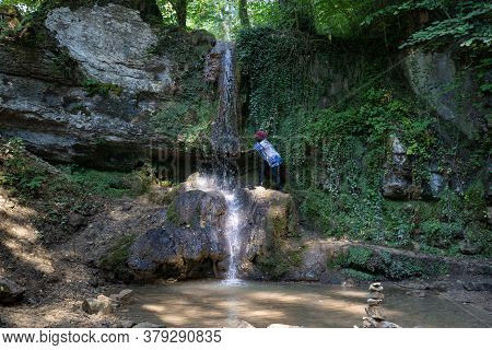 African Woman Climbs To The Water Of A Waterfall At A Hot Day In Summer. Linner Waterfall Is The Big