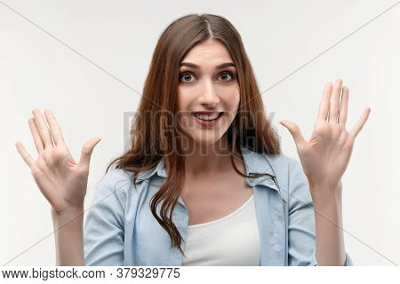 Studio Shot Of Surprised Young Female With Long Chestnut Hair, Dressed In Casual Clothes, Smiling Ha