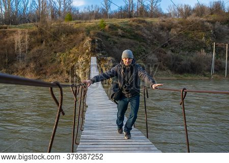 Autumn, A Man, A Photographer, Is Afraid And Runs Over A Swaying Suspension Bridge Over A River