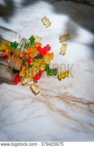 Assorted Flavors Of Gummy Bear Candies In Spilled Glass Jar On Marble Kitchen Table