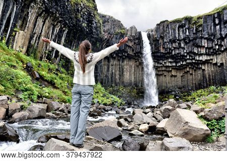 Iceland. Woman enjoying majestic Svartifoss waterfall. Female is visiting famous tourist attraction of Iceland. Spectacular natural landmark on vacation in Skaftafell. Icelandic nature landscape.