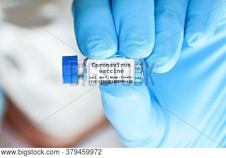 Hand In Blue Medical Gloves Holding Small Vial With Label Coronavirus Vaccine (sticker Own Design, D