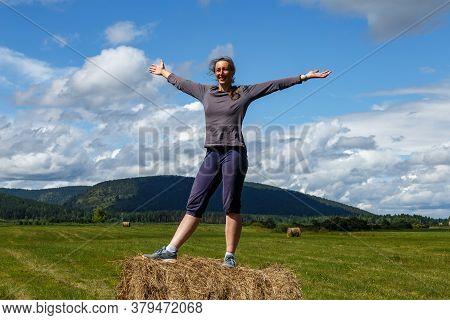 Vedenshina, Irkutskaya Oblast, Russia - July 30 2020: A Woman Stands With Arms Wide On A Haystack In