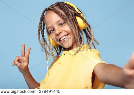 Positive Little Boy With African Dreads Wearing Headphones Taking Selfie With Smartphone Over Blue B