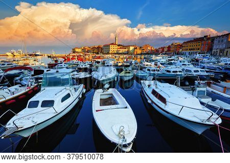 Rovinj, Istria, Croatia. Motorboats and boats on water in port Rovigno. Medieval vintage houses of old town. Yachts landing, high tower of Church of Saint Euphemia. Morning sunrise blue sky.