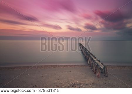 Wooden Breakwater In The Sea At Sunrise In Hindeloopen In Holland. The Sky Is A Blue Sky With Dramat