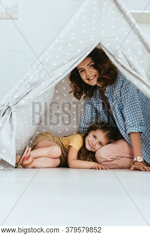 Kid Lying On Laps Of Smiling Nanny In Play Tent At Home