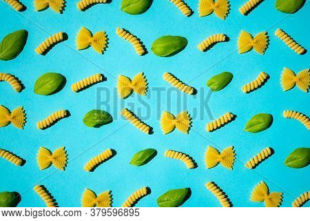 Uncooked Curly Pasta And Basil Leaf Pattern On Blue Background. Traditional Dry Raw Macaroni Pattern
