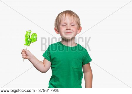 Child Boy 4 Years Old In A Green T-shirt Holds Lollipop Cock On Stick. The Kid Closed His Eyes Happi