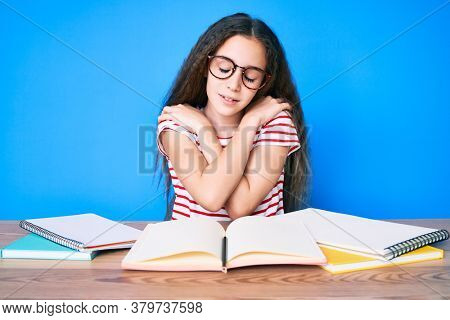 Cute hispanic child girl studying for school exam sitting on the table hugging oneself happy and positive, smiling confident. self love and self care 