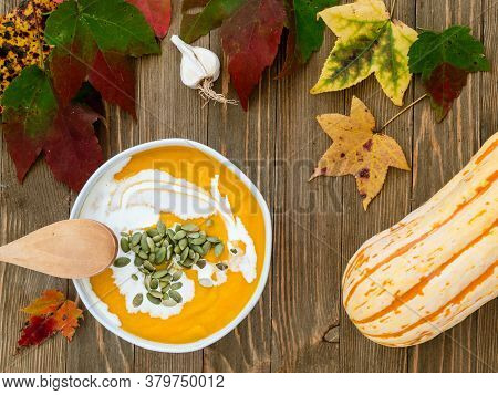 Bowl Of Winter Squash Soup Garnished With Pumpkin Seeds And Heavy Cream On A Rustic Wooden Table.