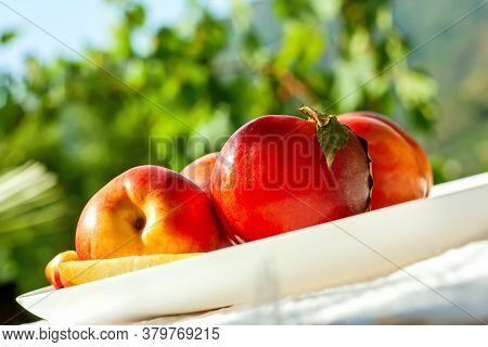Red Ripe Organic Nectarine Fruits On The White Plate On Nature Background. Summertime Healthy Eating