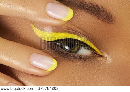 Close-up Female Eye With Bright Yellow Eyeliner Makeup. Neon Disco Make-up And Fashion Manicure. Sum