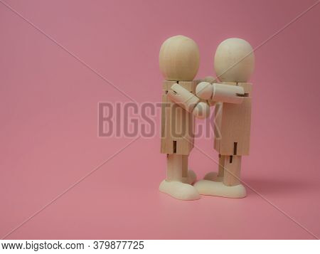 Wooden Dolls Hugging Each Other On A Pink Background.
Concept Of Social Contact From Wooden Dolls.