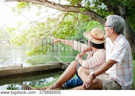 An Elderly Couple Hugging Each Other With Love And Happiness In A Park With A Large Pond. Senior Com
