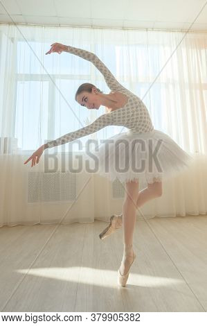 Beautiful Graceful Ballerina Is Practicing In The Hall Against The Background Of A Window. Slender W