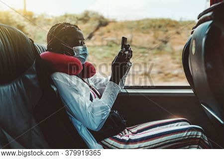 Side View Of A Black Woman Tourist Using A Smartphone On A Seat Of A Modern Regular Bus Near The Win