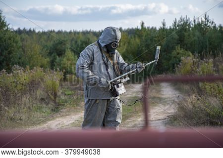 A Military Man In A Chemical Protection Suit Measures Radiation With A Dosimeter Standing In Front O