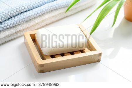 White Soap Bar On Wooden Soap Dish And Cotton Towels On White Counter Table In The Bathroom.