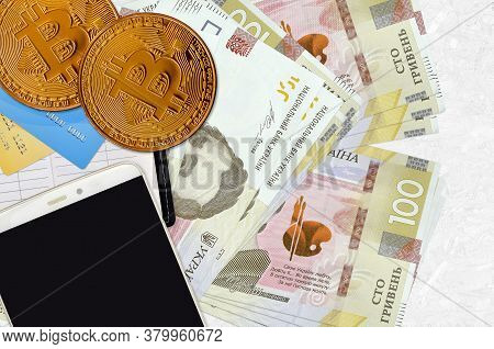 100 Ukrainian Hryvnias Bills And Golden Bitcoins With Smartphone And Credit Cards. Cryptocurrency In