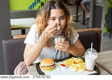 Asian Young Girl Sitting At Table Indoors And Eating Ice Cream. Fart Her  Hamburger, Fries, Ketchup 