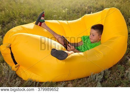 Little Boy Lies In A Lamzak, Holding A Smartphone Or Tablet In His Hands, Plays Or Communicates On S