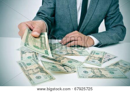 man in suit sitting in a desk full of dollar bills offering one of them to the observer