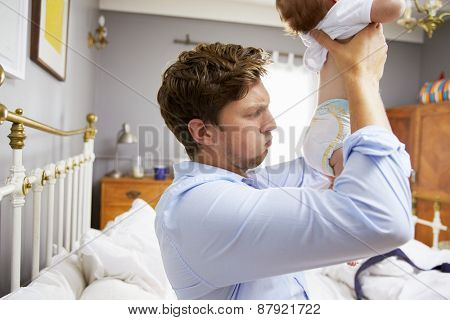 Father Dressed For Work Changing Baby's Diaper In Bedroom