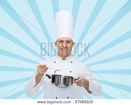 cooking, profession and people concept - happy male chef cook with pot and spoon over blue burst rays background