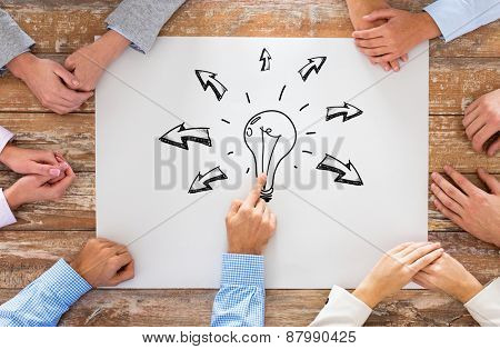 business, people, idea, inspiration and team work concept - close up of creative team sitting at table and pointing finger to bulb doodle on paper in office