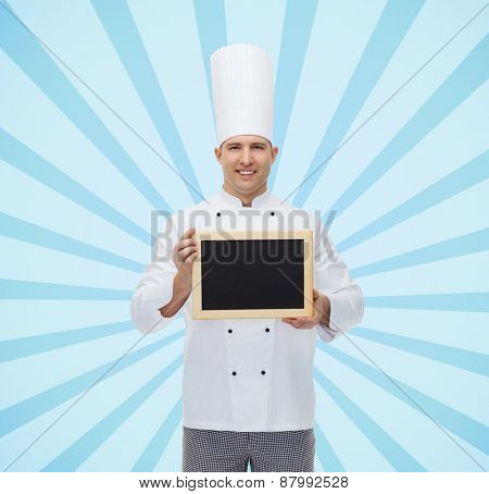 cooking, profession, advertisement and people concept - happy male chef cook showing and holding blank menu board over blue burst rays background