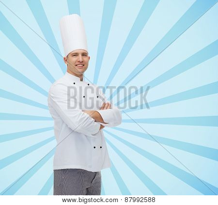 cooking, profession and people concept - happy male chef cook with crossed hands over blue burst rays background