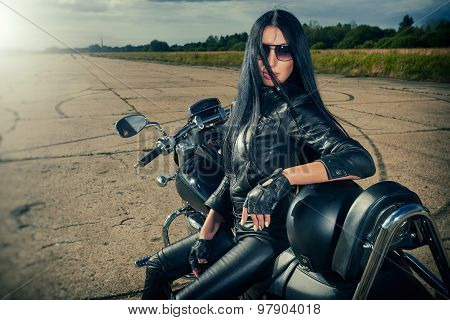 Biker girl in leather jacket sitting on a motorcycle.