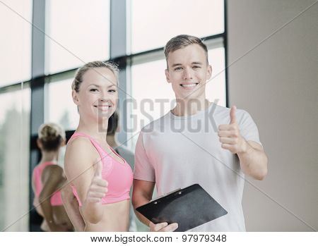 fitness, sport, exercising and diet concept - smiling young woman with personal trainer in gym showing thumbs up