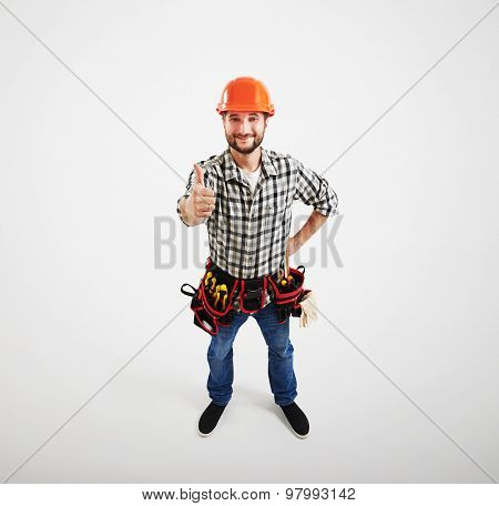 view from above of smiley builder in hard hat and belt with tools looking up and showing thumbs up. isolated on light grey background