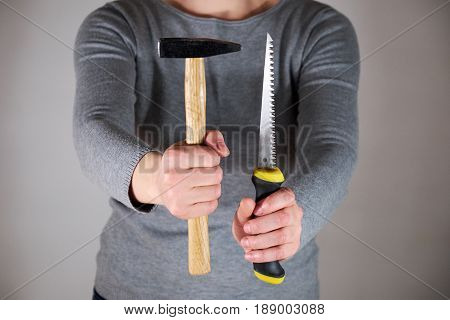 Woman holding saw and hammer in two hands