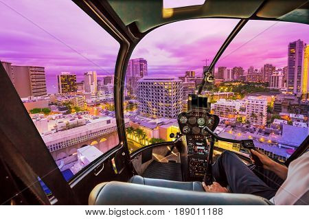 Pink light at twilight of Waikiki cityscape in Oahu island, Hawaii, United States. City night lights and nightlife concept. Helicopter cockpit with pilot arm and control console inside the cabin.