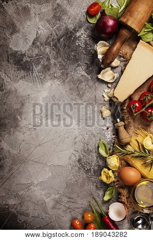Italian food background with vine tomatoes, basil, spaghetti, spinach, onion, parmesan, olive oil, garlic, peppercorns, rosemary and eggs. Slate background 