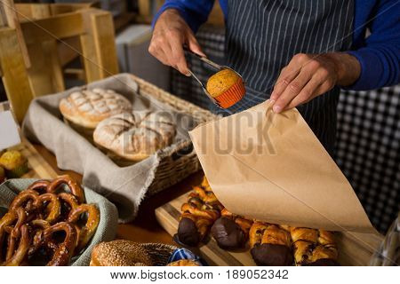 Mid section of staff packing cup cake in paper bag at counter in bakery shop