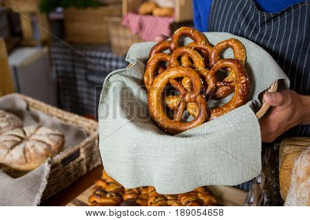 Mid section of staff holding wicker basket of pretzel breads at counter in bakery shop