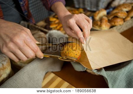 Mid section of staff packing cup cake in paper bag at counter in bakery shop