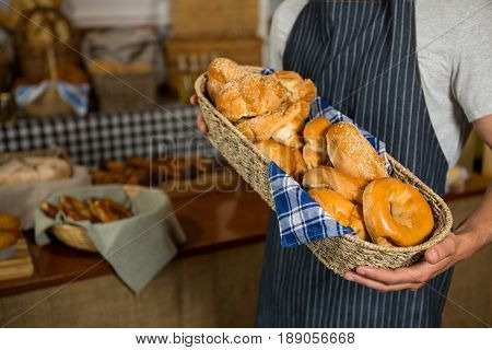 Mid section of male staff holding wicker basket of various breads at counter in bakery shop