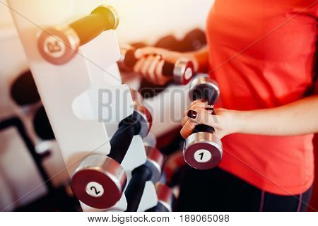 Sports equipment dumbbell rests in a row, girl takes a dumbbell in the gym. hands close-up. hign contrast and monochrome color tone