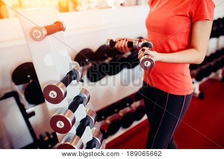 Sports equipment dumbbell rests in a row, girl takes a dumbbell in the gym. hands close-up. hign contrast and monochrome color tone