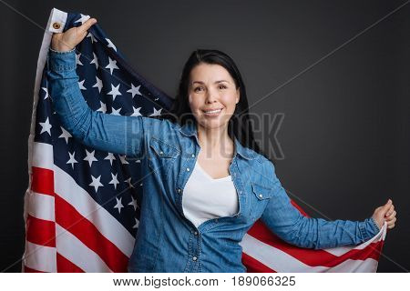 Long live my country. Magnificent optimistic inspiring woman making a photoshoot in a studio while feeling patriotic and posing with the national flag