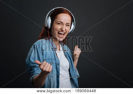 Amazing playlist. Cute gorgeous enthusiastic woman testing her new headphones by playing her songs while standing isolated on grey background