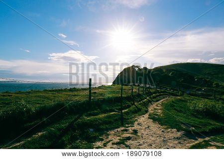 Sunlight over green fields and coastal path near West Lulworth village in Dorset, Jurassic Coast, England