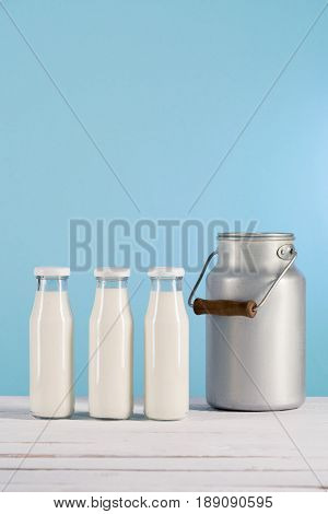 Row Of Glass Bottles With Milk On Tabletop With Can At Blue Background