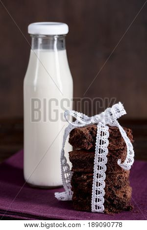 Glass Bottle Of Milk With Brownie Cakes With White Ribbon On Napkin At Tabletop